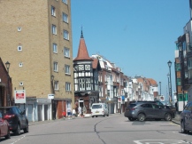Street with cars lined on it. A variety of old and new buildings on it.